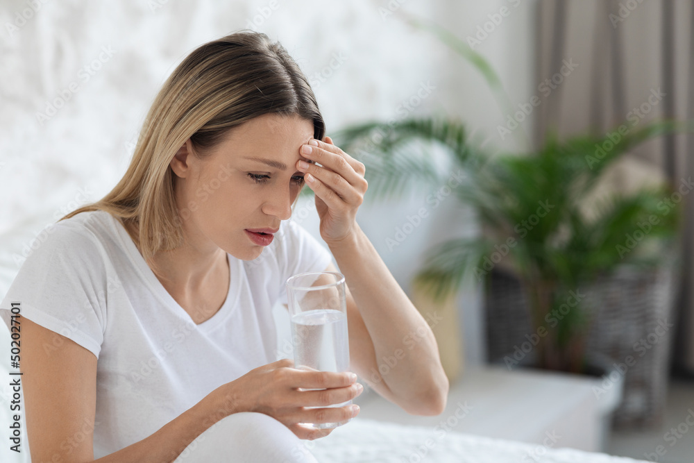Sick blonde lady feeling bad, touching head, bedroom interior Sick blonde lady feeling bad, touching head, bedroom interior