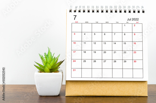 July 2022 desk calendar with plant on wooden table.