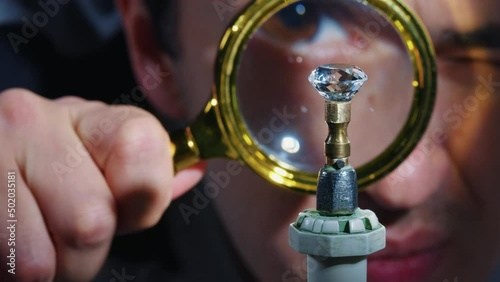 Appraiser looks through magnifying glass at gemstone turning on metal dop stick. Expert man is trying to determine cost, authenticity, value of precious gem after jewelry cutting with loupe photo