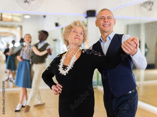 Slika na platnu Elderly woman learning ballroom dancing movements in pair