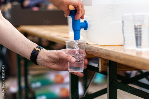 Water in the cooler. The girl pours water from the cooler into a plastic cup. Water in a plastic cup. Liquid in the cooler.