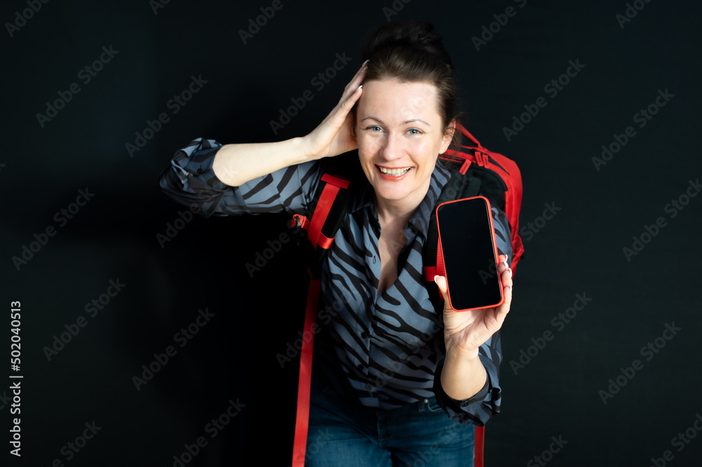 Cheerful woman with red backpack showing cellphone empty screen isolated on black background Cheerful woman with red backpack showing cellphone empty screen isolated on black background