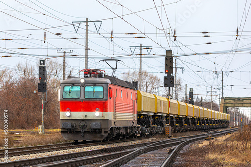 A red locomotive with a long freight train is going to the railway station. Freight railway transportation of goods. Winter weather.