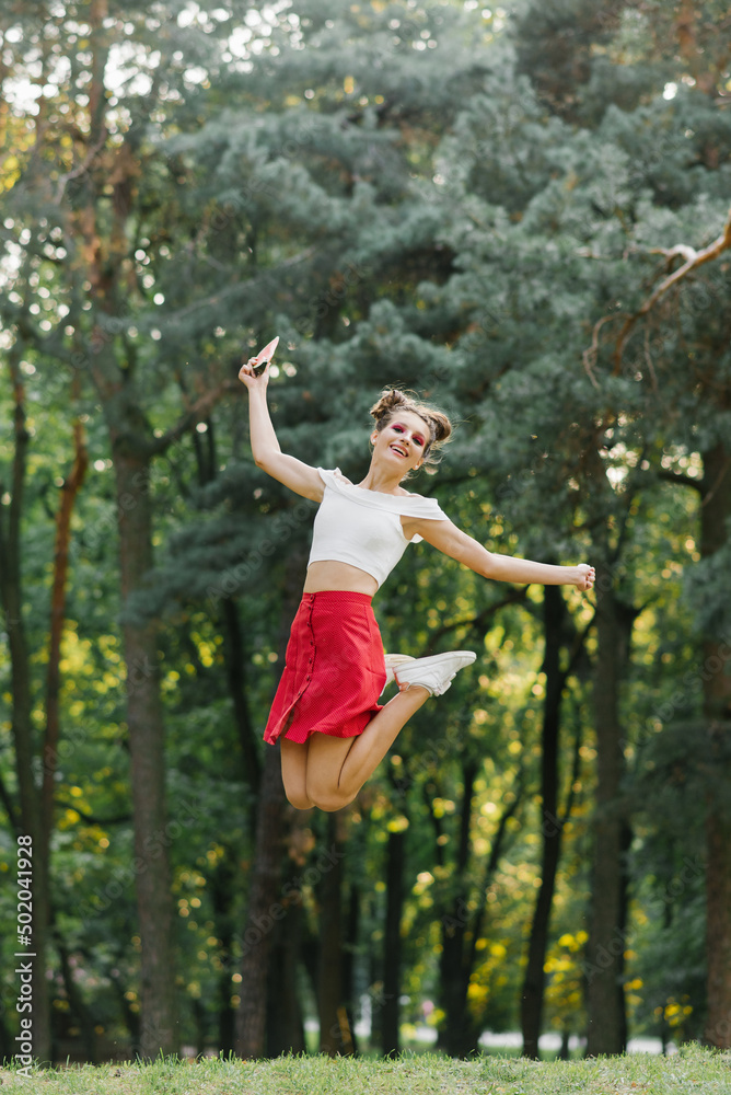 A young happy woman in a red skirt jumps high in a summer park, having fun