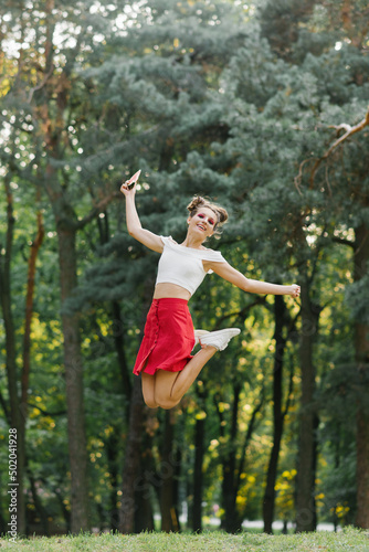 A young happy woman in a red skirt jumps high in a summer park  having fun