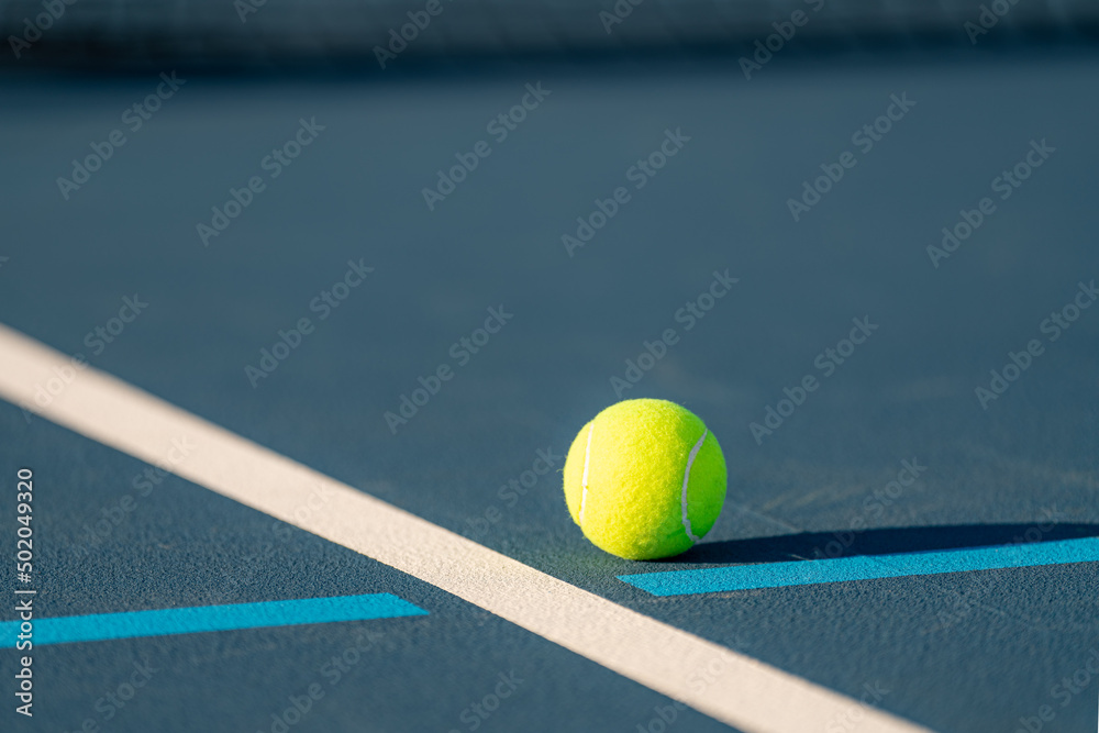 Yellow tennis ball on blue tennis court with white lines and light blue pickleball lines.