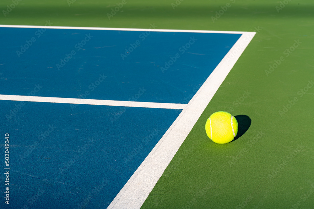 Yellow tennis ball at blue tennis court with white baseline and green out of bounds