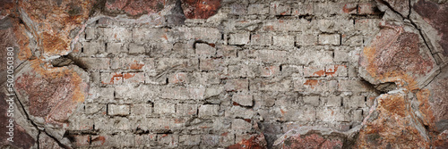 Old brick wall with chipping natural stone cladding. Vintage brickwork texture. Grunge background with space for design. Rough dirty distressed surface. Broken facade of the building. Wide banner.