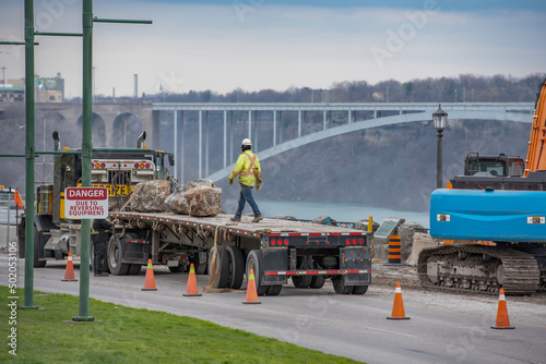 Foto Construction worker on back of a semi truck with flatbed trailer loaded with large landscaping boulders