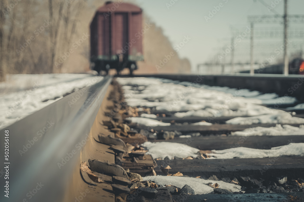 Close-up of old railway nails to attach rails to wooden sleepers. Blurred freight wagon stands on the spare track of the railway. Selective focus