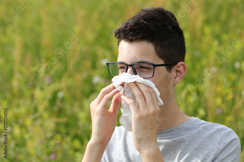 Fotografia allergic guy with glasses sneezing on a white handkerchief