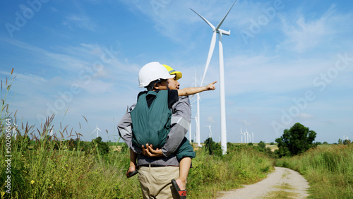 engineer father and his son playing Piggyback in a wind turbine field, father teaching his son how to live in harmony with nature and technology, family relationships.