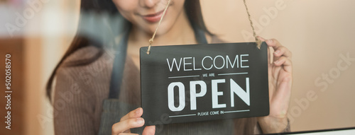 beautiful female business retail owner  hanging open wooden sign board at the entrance door of the shop and ready to service customer.