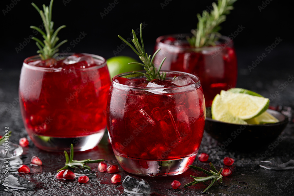 Pomegranate gin cocktail with lime, rosemary and ice on rustic black table Pomegranate gin cocktail with lime, rosemary and ice on rustic black table