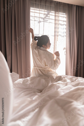 white dress asian female beautiful woman stretching morning wake up freshness and carefree weekend moment in cosy interior bedroom with white curtain and sun shine background lifestyle home concept