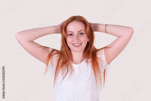 smiling redhead young woman with tousled hair stretches on a light background