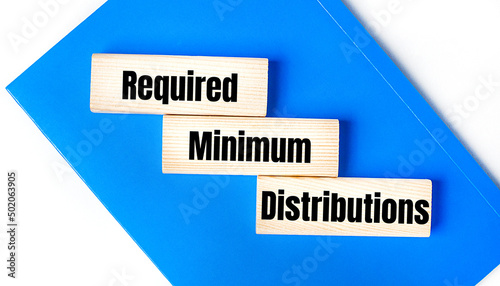 There is a blue notebook on a light gray background. Above are three wooden blocks with the words RMD Required Minimum Distributions photo