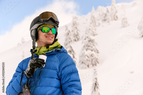 portrait of young smiling man in ski goggles against the background of snow-capped mountains.