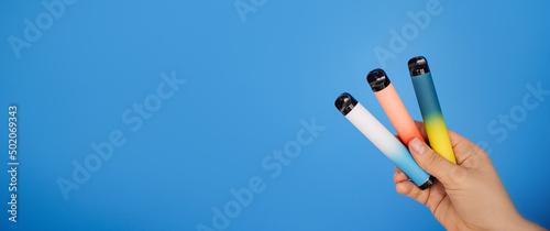 Disposable three electronic cigarettes in a woman's hand close-up on a blue background. The concept of modern smoking, vaping and nicotine. Space for text