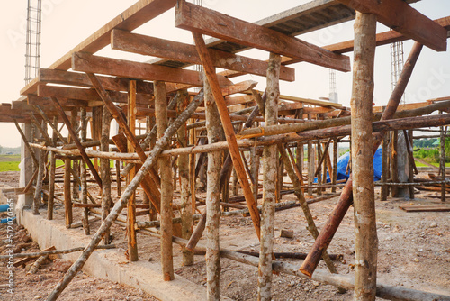 Temporary poles and wooden scaffolding support concrete beams at the house construction site. © Montree