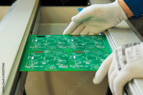 White gloved hands install the PCB into the feed line on the PCB Installer. Production of printed circuit boards.