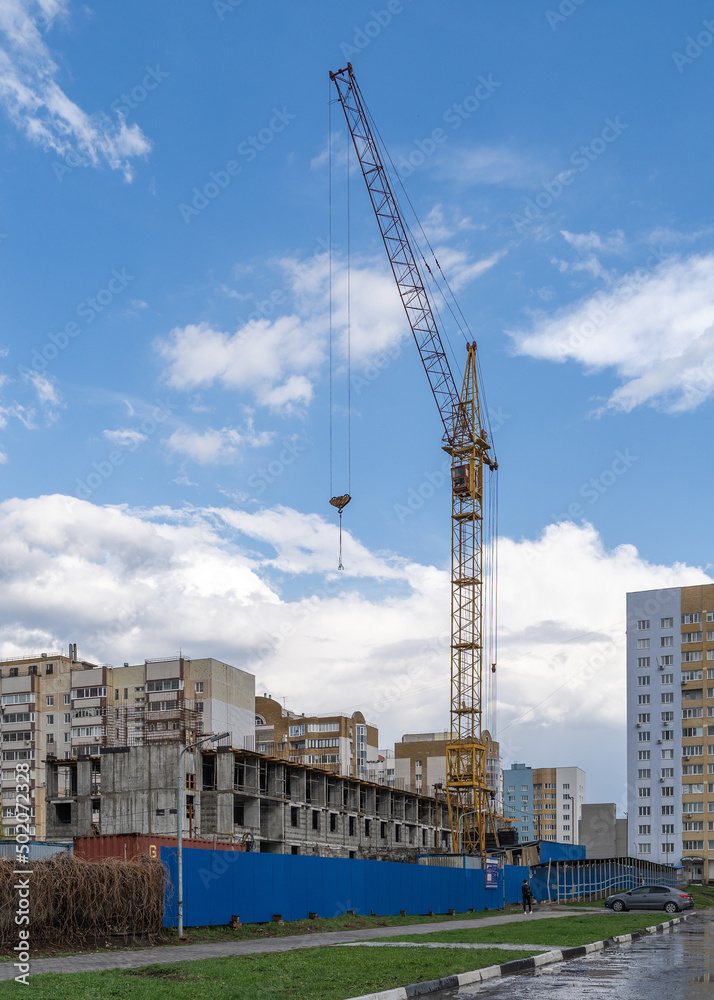High-rise crane on the construction of a multi-apartment high-rise residential building in the city on the street.