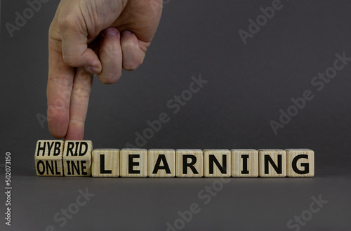 Online or hybrid learning symbol. Businessman turns cubes, changes words online learning to hybrid learning. Grey background. Business, educational and online or hybrid learning concept. Copy space.