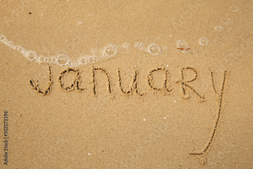 January - handwritten on the soft beach sand.