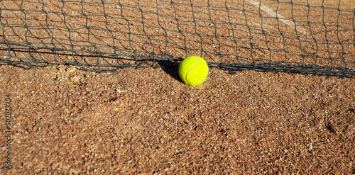 Tennis yellow ball on a clay court near the net. Tournaments. Sports backgrounds. Copy space for text. © LKoroleva