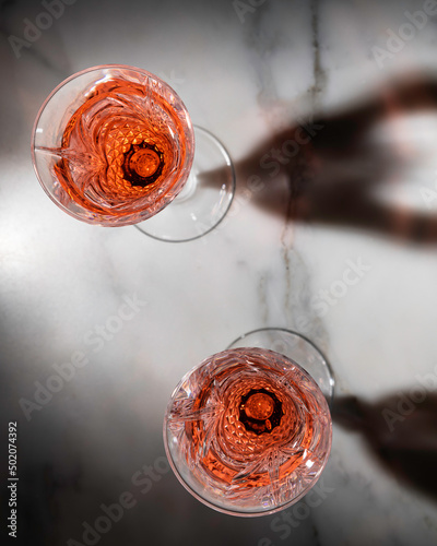 Rose wine in fancy crystal flutes on rich Carrera marble background with creative shadow effect.