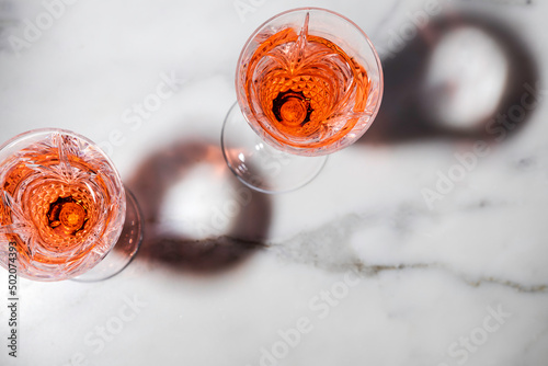 Rose wine in fancy crystal flutes on rich Carrera marble background with creative shadow effect.