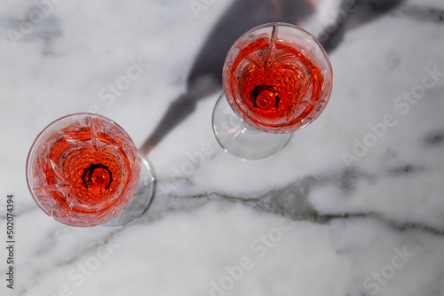 Rose wine in fancy crystal flutes on rich Carrera marble background with creative shadow effect.