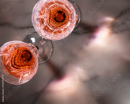 Rose wine in fancy crystal flutes on rich Carrera marble background with creative shadow effect.