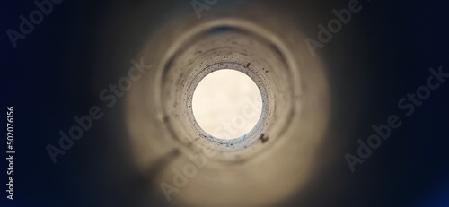 Close-up deep endless round large and long concrete pipe hole with blurry black foreground and white background with copy space. Bore well, drainage, pipeline, mining and factory sewage concept.