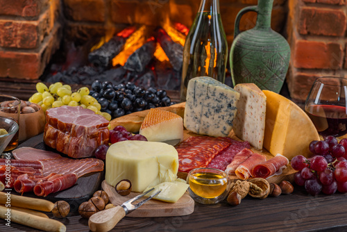 Charcuterie plate board, meat, boiled pork, smoked meats, prosciutto, and wine. Cheese pieces, nuts, grapes, honey on a wooden table. Refreshments and tasting alcoholic drinks in the wine cellar