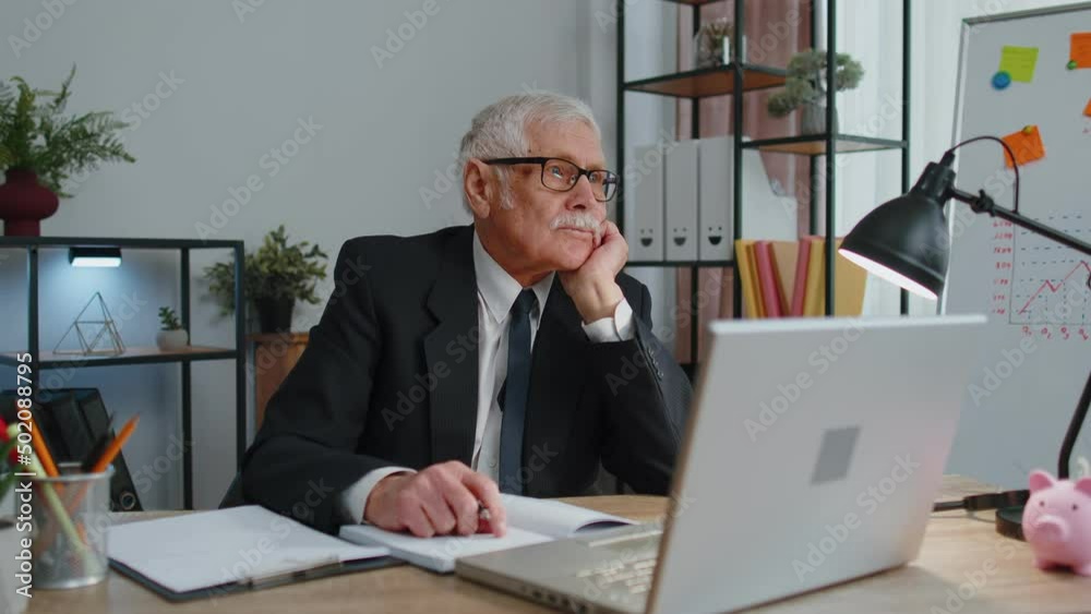 Senior business office man freelancer wears glasses using laptop computer, analyzes financial charts celebrate success win scream rejoices doing winner hands gesture say Yes sits at workplace desk Senior business office man freelancer wears glasses using laptop computer, analyzes financial charts celebrate success win scream rejoices doing winner hands gesture say Yes sits at workplace desk