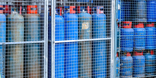 Quadro su tela Group of blue colored propane gas cylinders with red handle behind metal bolt an