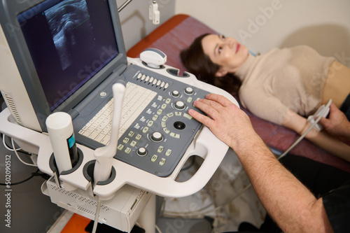 Focus on the hand of a doctor radiologist examining female patient on modern ultrasound machine. USG ultrasonography