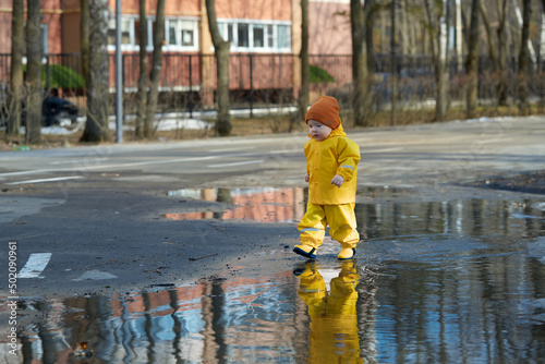 a kid in a yellow waterproof suit walks through puddles