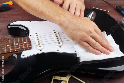 Guitar master wipes surface of black electric guitar with rag.