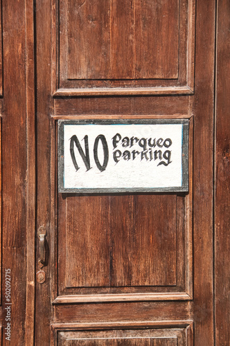 No parking sign on a brown wooden doorframe in both english and spanish language, stylish and relaxed sign