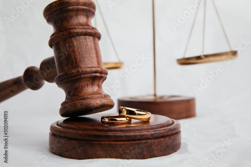 Wooden judge gavel with rings close-up on light background. Family, divorce and law concept photo