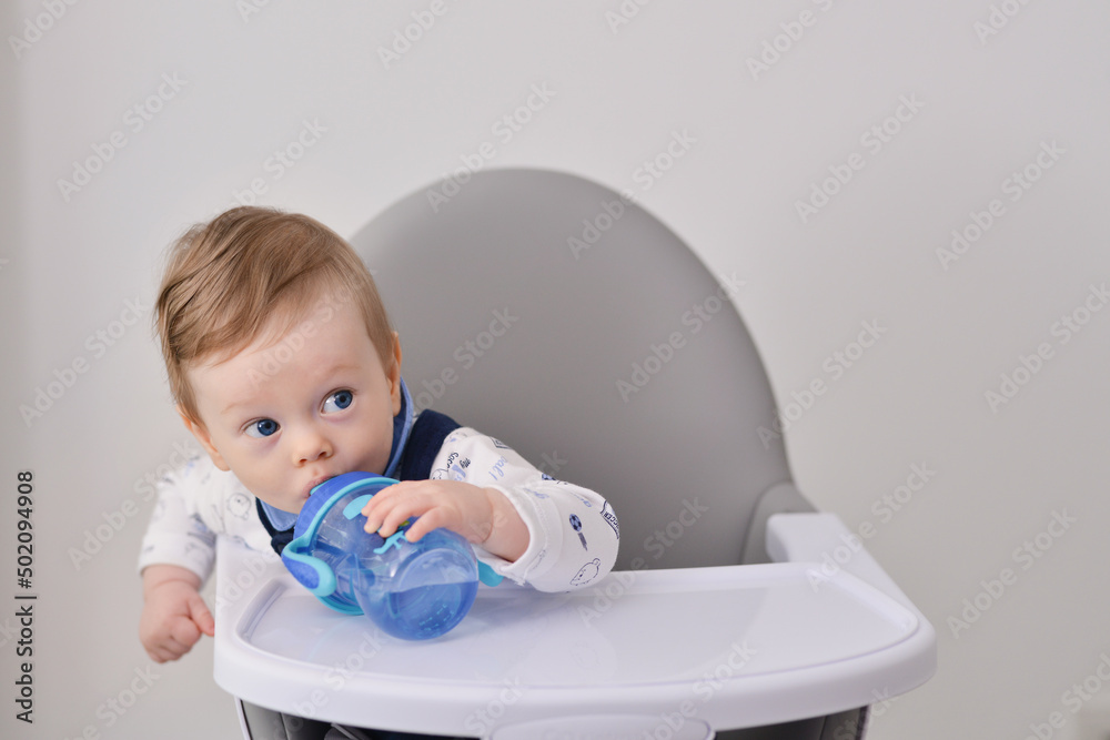 Sweet baby boy holding bottle and drinking water. Baby drinking water from bottle sitting in the high chair. Baby holding bottle Sweet baby boy holding bottle and drinking water. Baby drinking water from bottle sitting in the high chair. Baby holding bottle