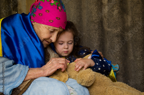 A grandmother with a child hides in the basement during the war. The child is wrapped in a Ukrainian flag in a bomb shelter. War in Ukraine. Stop war. A woman with a child in a bomb shelter. 