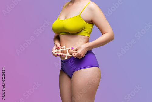 Beauty woman in underwear measuring her body fat with caliper on a purple background with a gradient