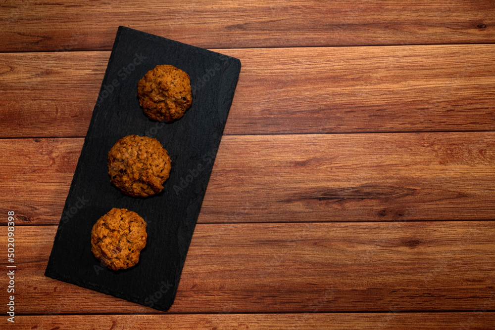 Cookies with pieces of chocolate on dark slate plate, light wood background. Top view, flat lay, space for text.