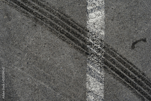 Asphalt texture with white line and tire marks. Smooth asphalt road. Tarmac dark grey grainy road background.Top view