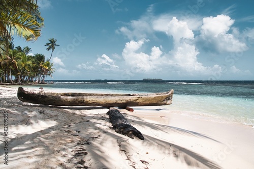 Small traditional boat of indigenious people lying on a white sand beach at a small island in Panama with palm trees in the background creating a calm paradise like scene photo