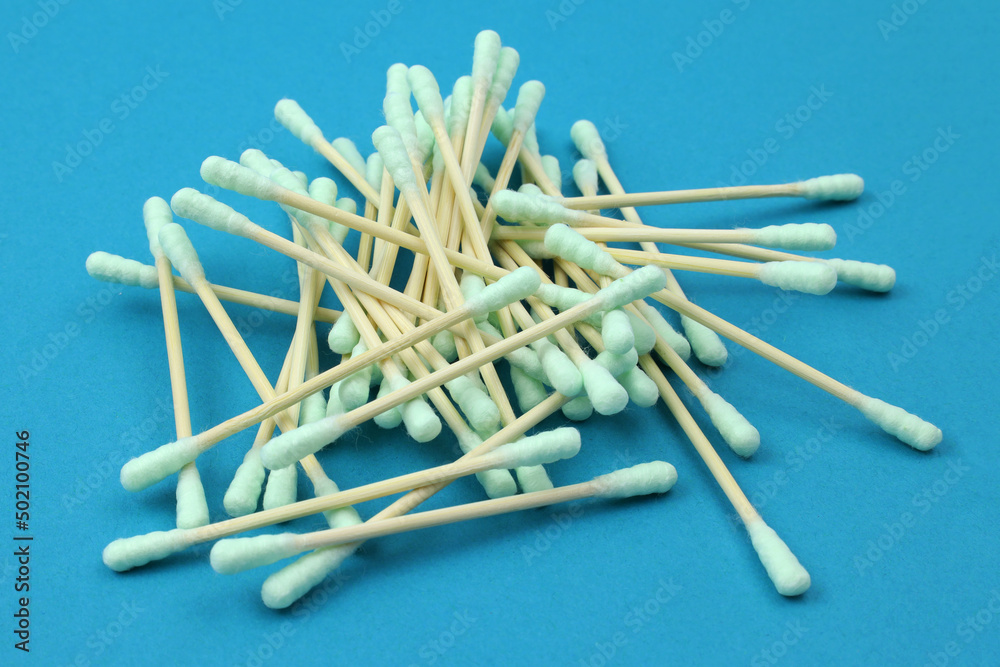 Cotton ear buds, wooden stick. Ear cleaner - Pile of green cotton buds. Set of ear cotton sticks on blue background Cotton ear buds, wooden stick. Ear cleaner - Pile of green cotton buds. Set of ear cotton sticks on blue background