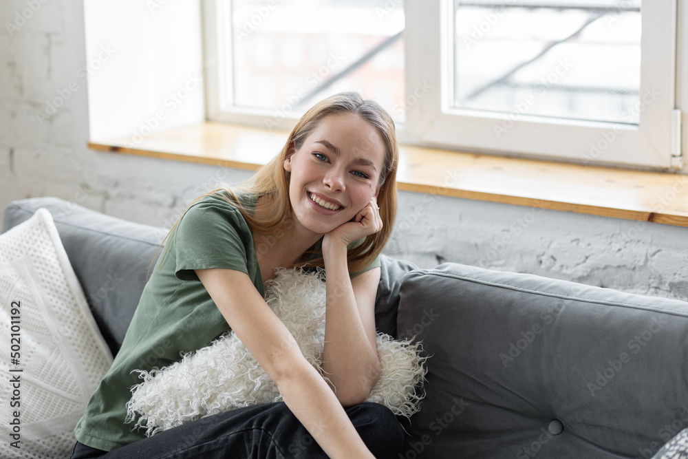 Young beautiful millennial girl sitting on the sofa, smiling Young beautiful millennial girl sitting on the sofa, smiling